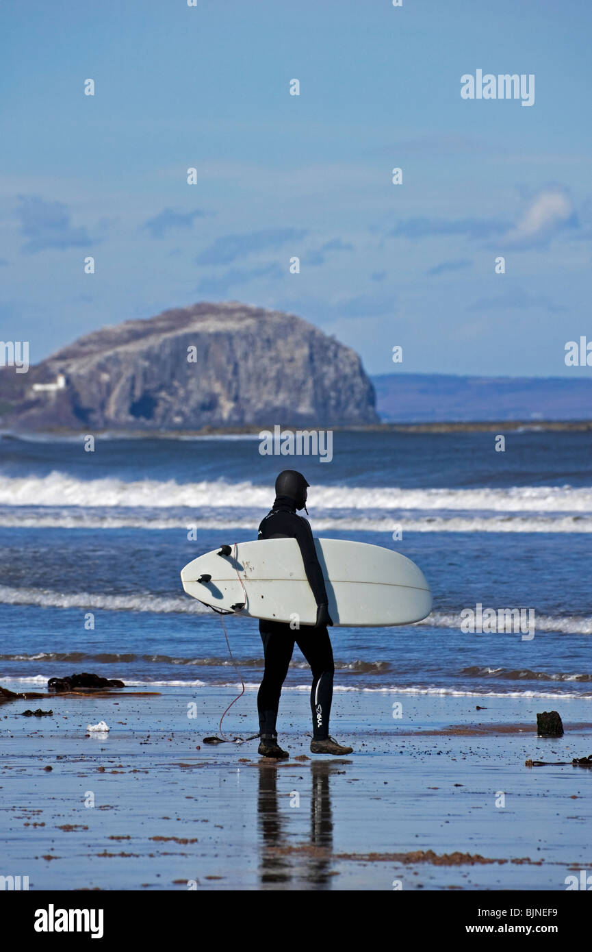 One male surfer walking towards the waves on a sunny day, Belhaven Bay beach, East Lothian, Scotland, UK, Europe Stock Photo