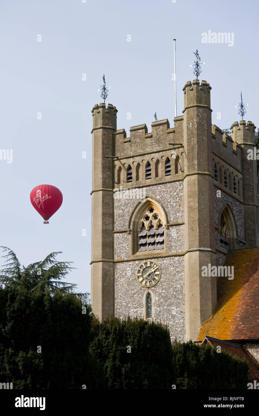 Virgin hot air balloon passing near to the church tower of St Mary the Virgin parish church of Hambleden Buckinghamshire UK Stock Photo