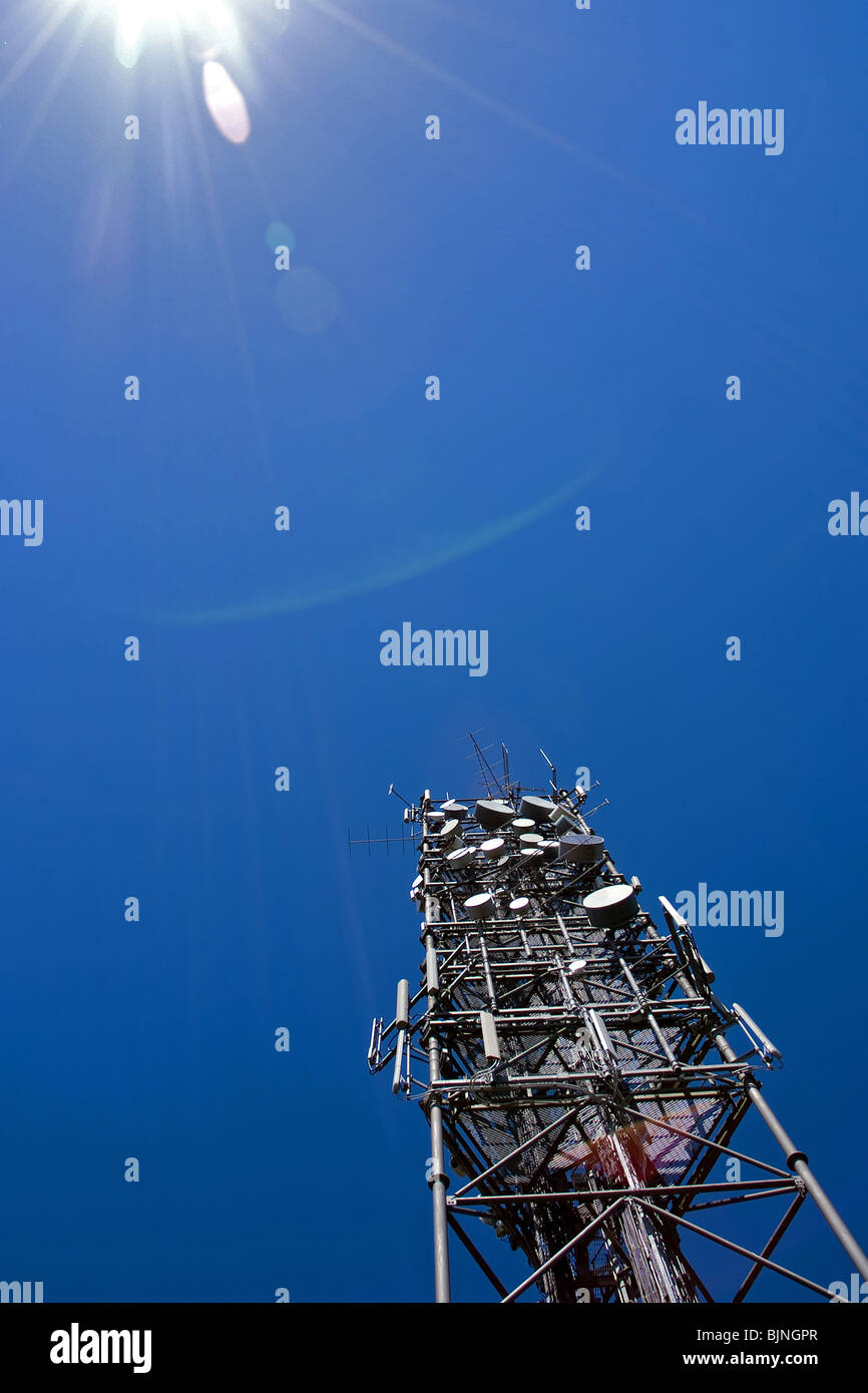 A large communications mast against blue shy with the sun in shot Stock Photo