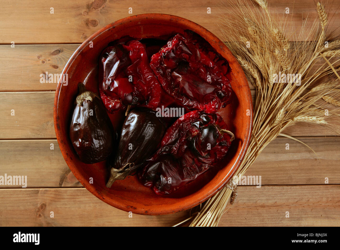 Eggplant and peppers roasted with wheat ear spike on wooden table Stock Photo