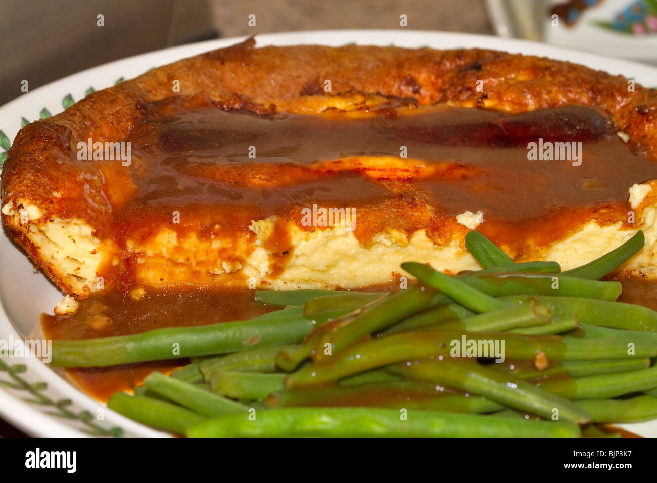 Toad in the hole, traditional British dish of sausage and yorkshire pudding with gravy and green beans Stock Photo