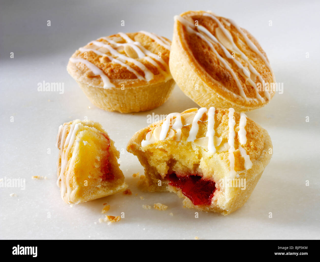 Traditional almond flavoured individual bakewell tarts, on broken open to see filling, on a white background Stock Photo