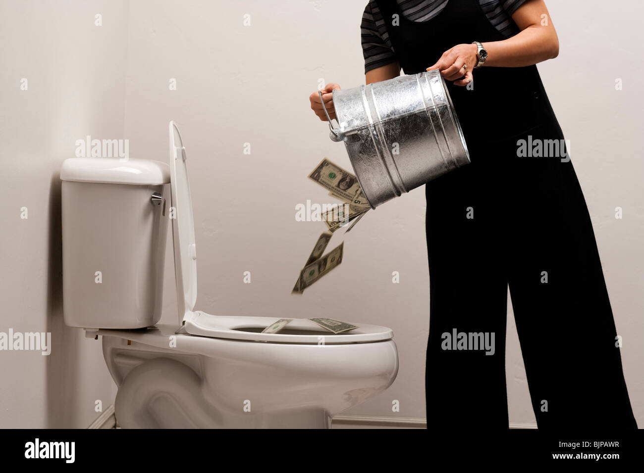A person pouring a bucket of money down the toilet Stock Photo