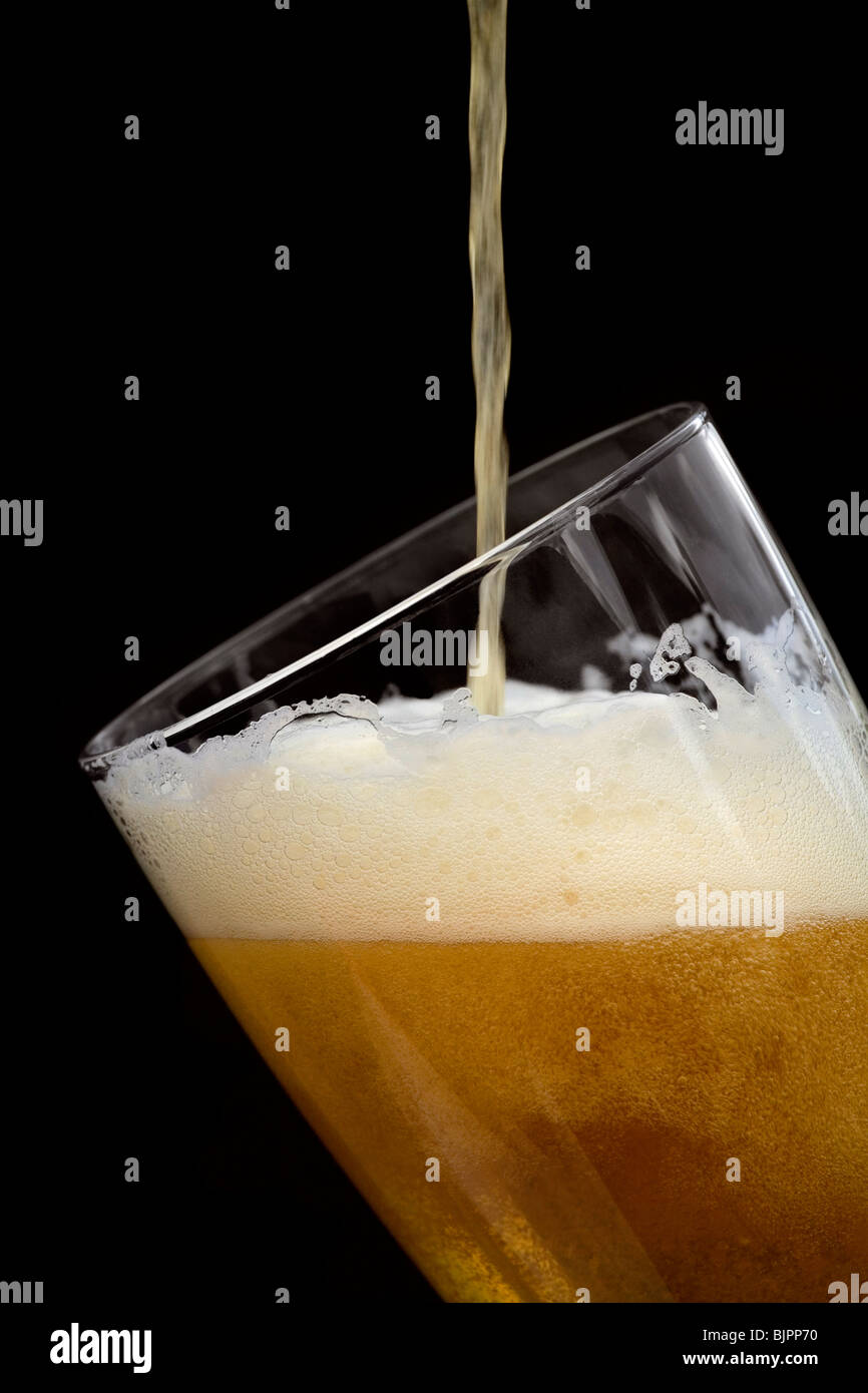 Lager or beer being poured slowly into a glass and showing the bubbles and froth. All shown against a black background Stock Photo
