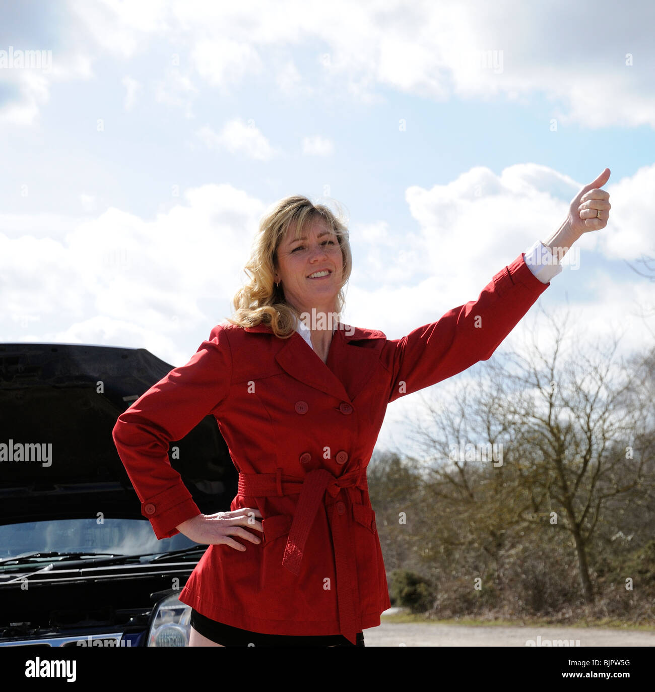 Woman motorist standing by broken down car thumbing a lift on the roadside Stock Photo