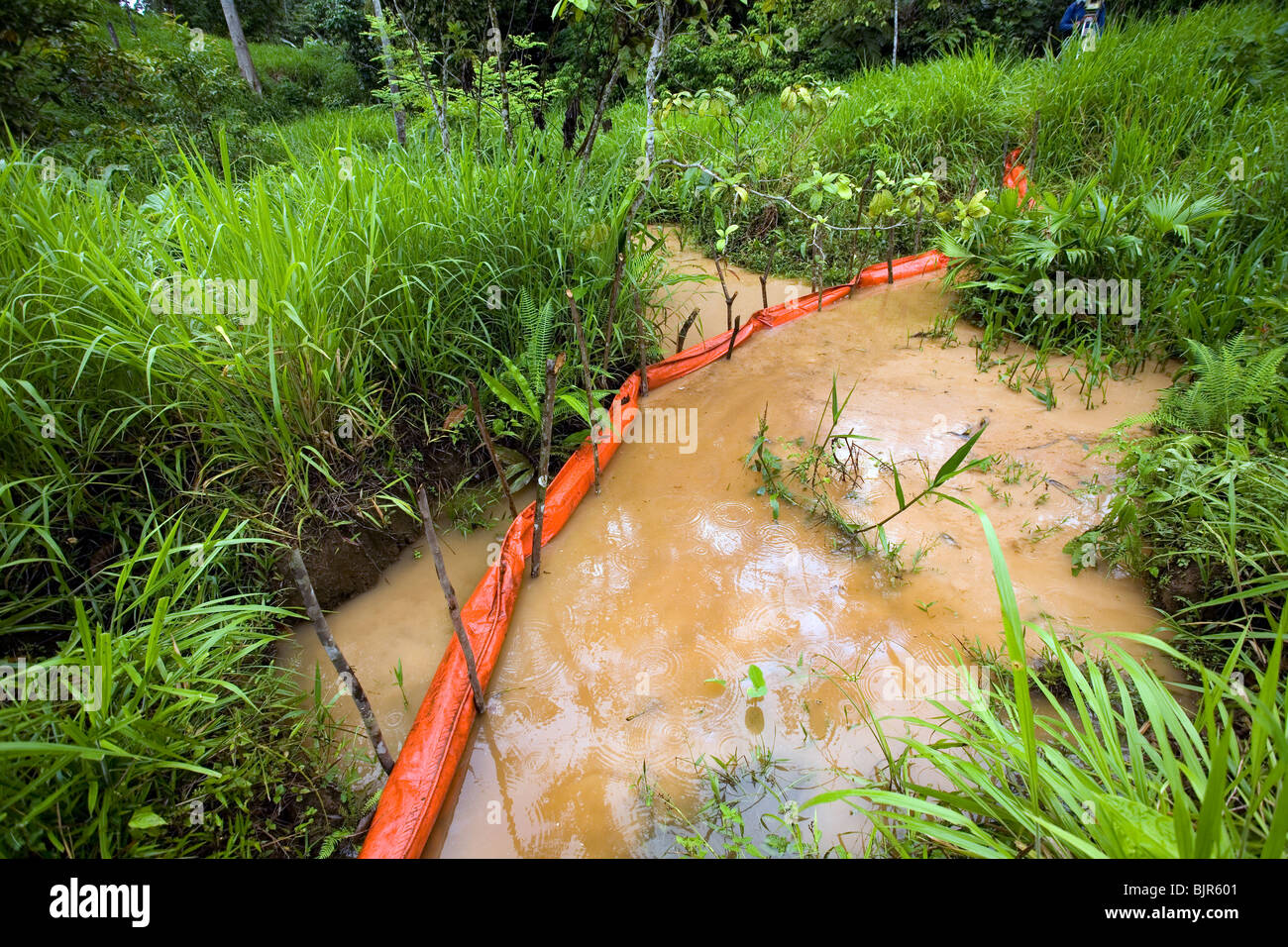Oil spill in an Amazonian stream with boom in position to contain slick. Stock Photo