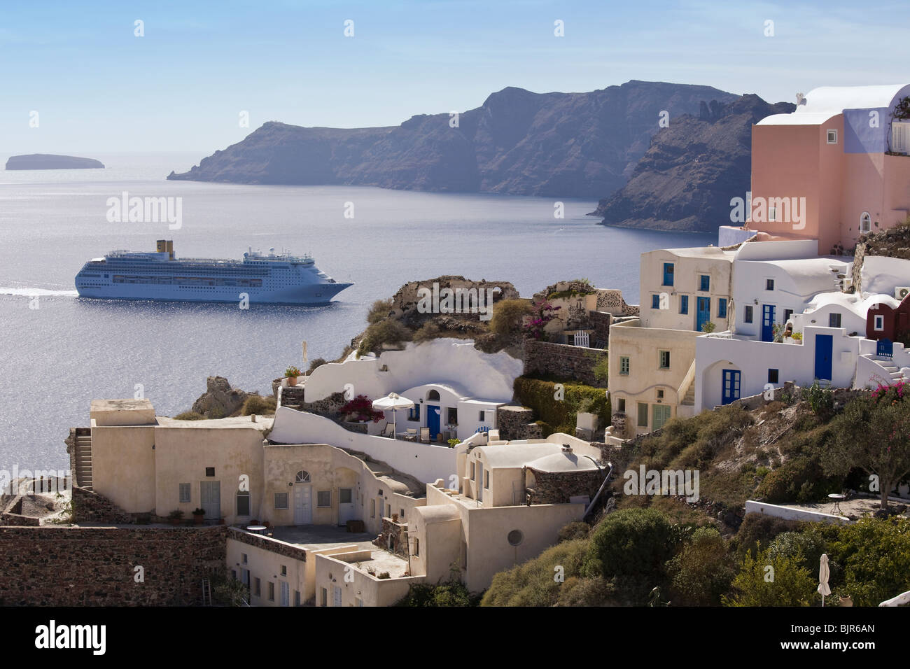 Cruise ship leaving caldera of Santorini past village of Oia. Stock Photo