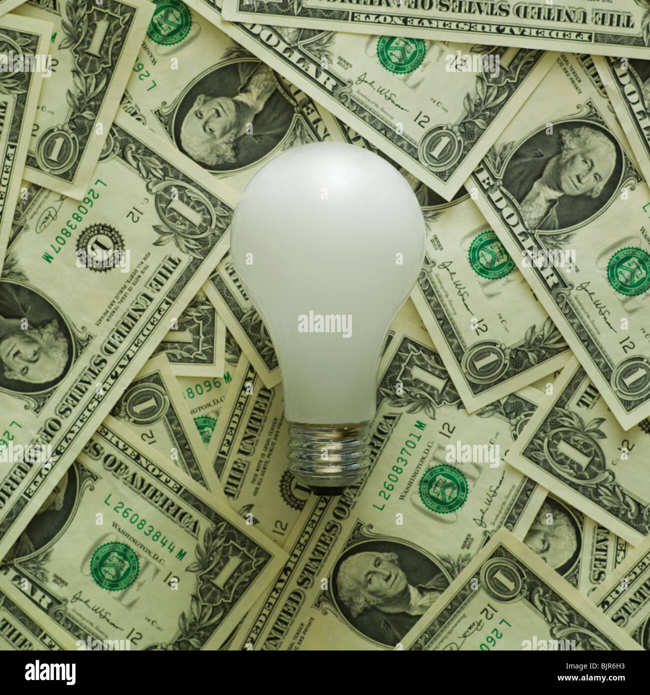 light bulb on a pile of dollar bills Stock Photo