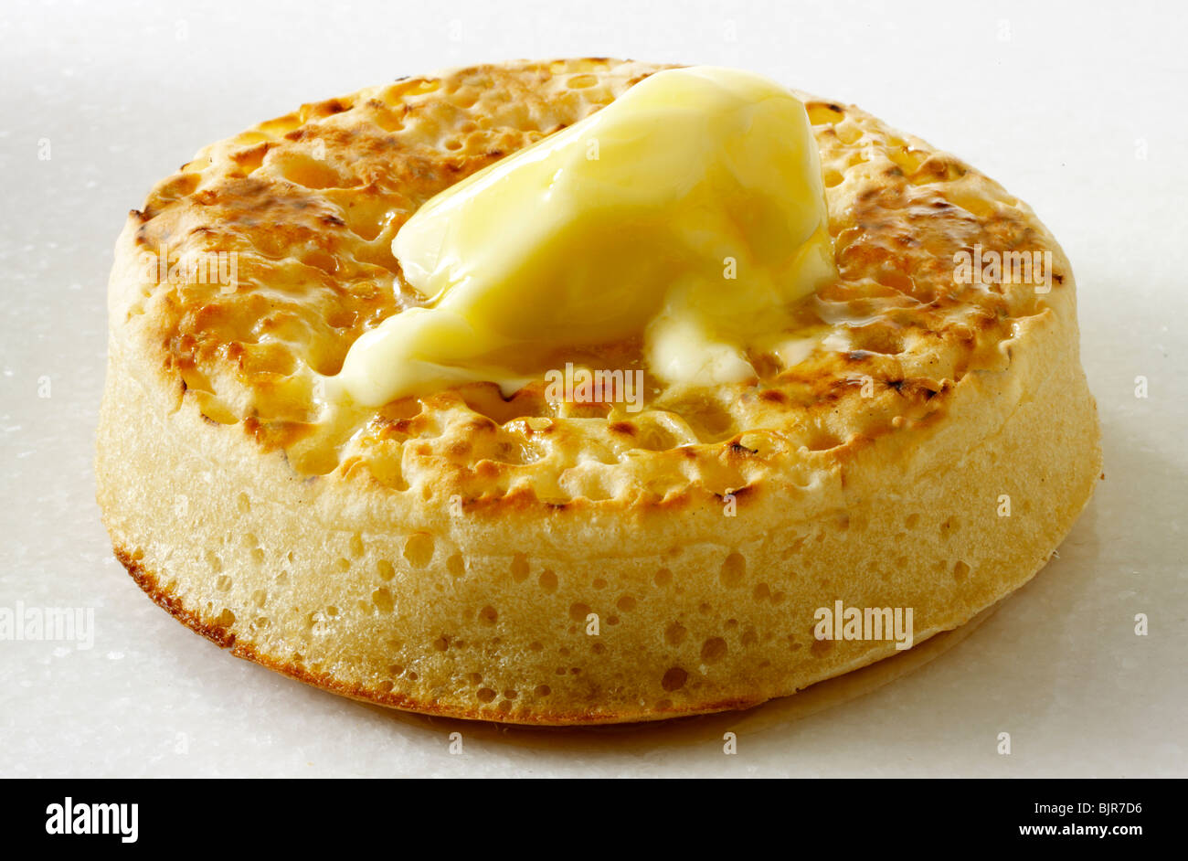 Single traditional hot buttered crumpet close up on a white background, with melted butter ready to eat Stock Photo