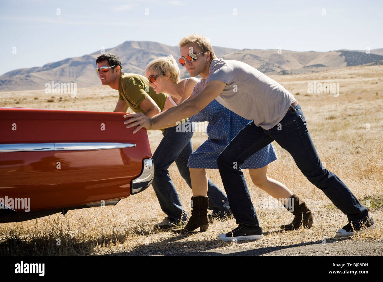 people pushing a car down the road Stock Photo