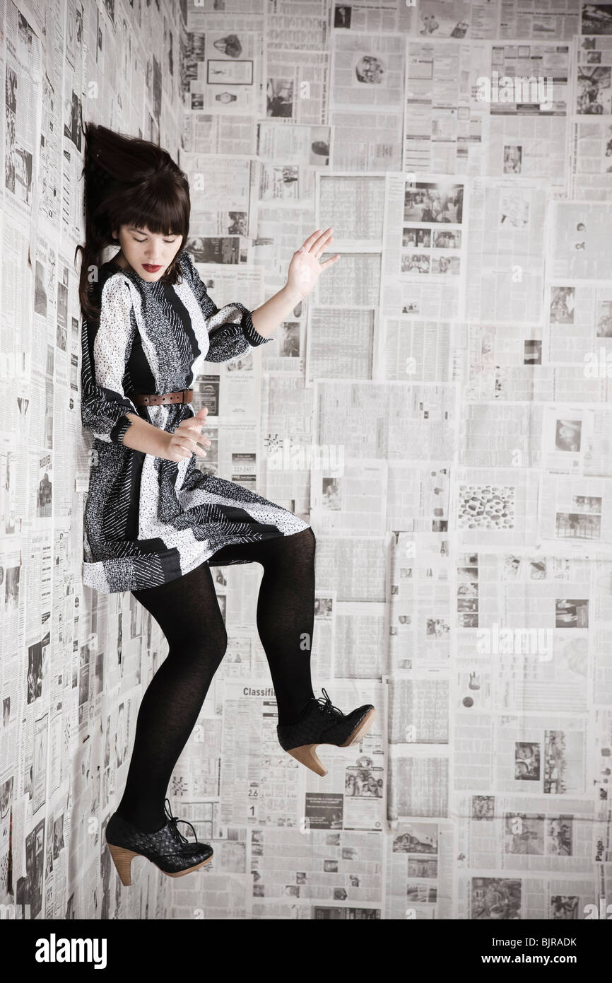 Young woman stuck to wall covered with newspapers, studio shot Stock Photo  - Alamy