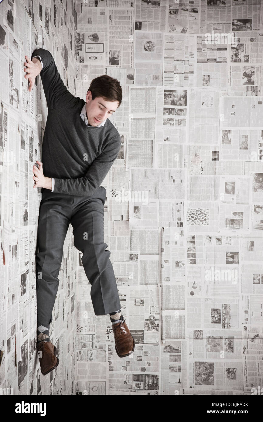 Young man stuck to wall covered with newspapers, studio shot Stock Photo