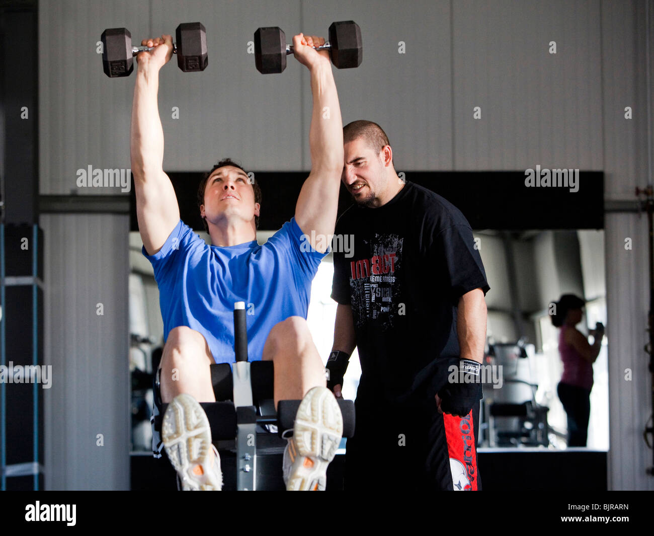 Instructor assisting man exercising in gym Stock Photo