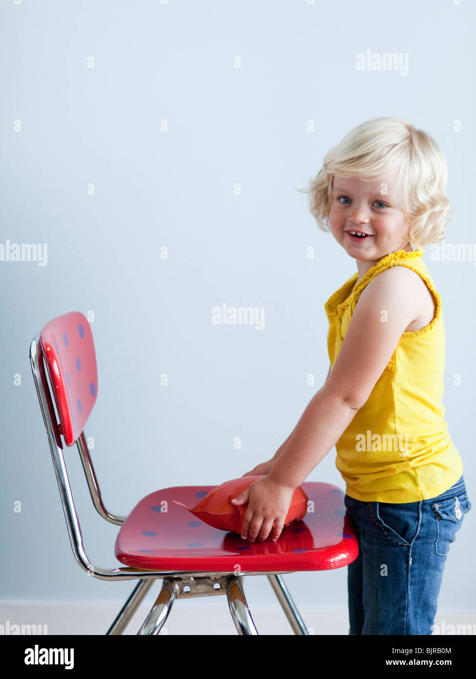 Girl (2-3) putting whoopie cushion on chair, smiling, studio shot Stock Photo