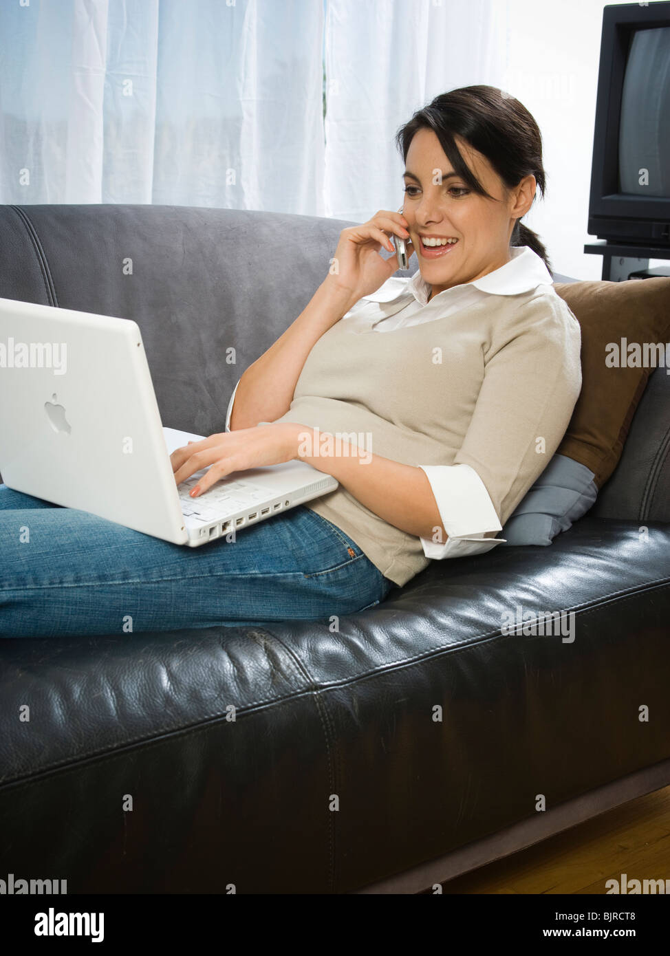 USA, Utah, Orem, woman lying on sofa using laptop and cell phone Stock Photo