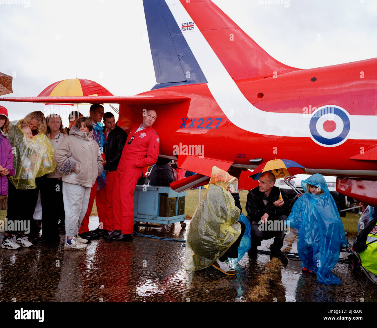 Red Arrows pilots shelter from rain storm under tail of a BAE Systems Hawk at Kemble Air Day. Stock Photo