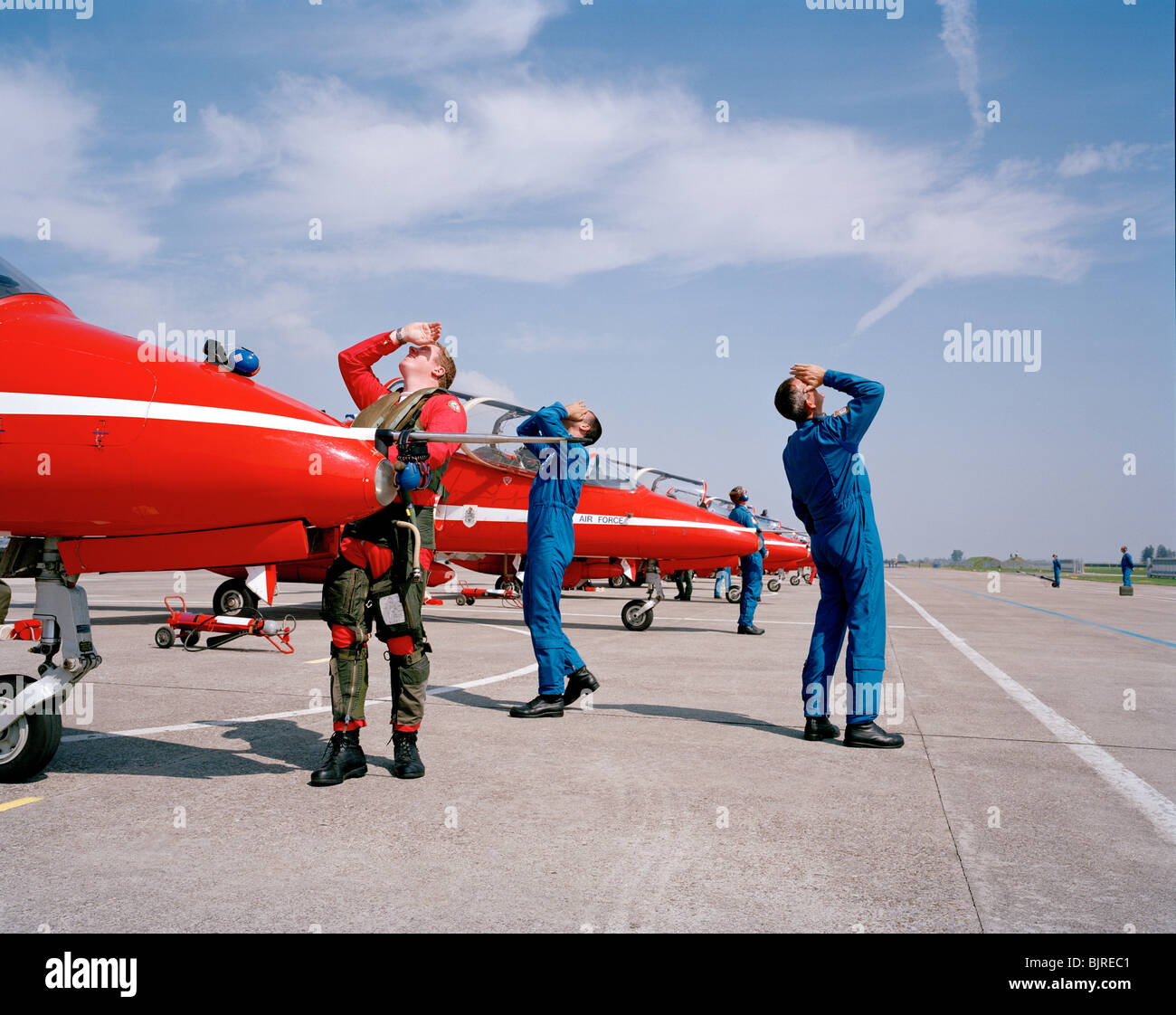 Support team members and a pilot of the aerobatic RAF Red Arrows team, watch others displaying above their heads. Stock Photo
