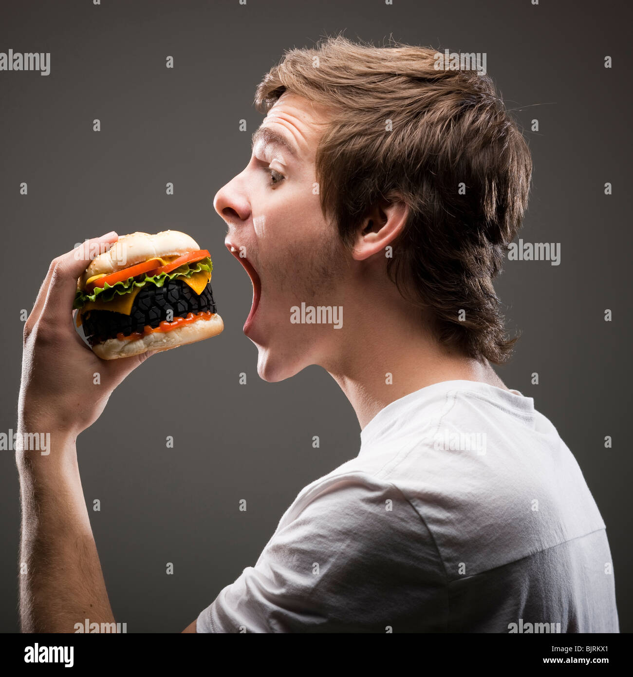 Side view of young man about to bite a tire hamburger Stock Photo