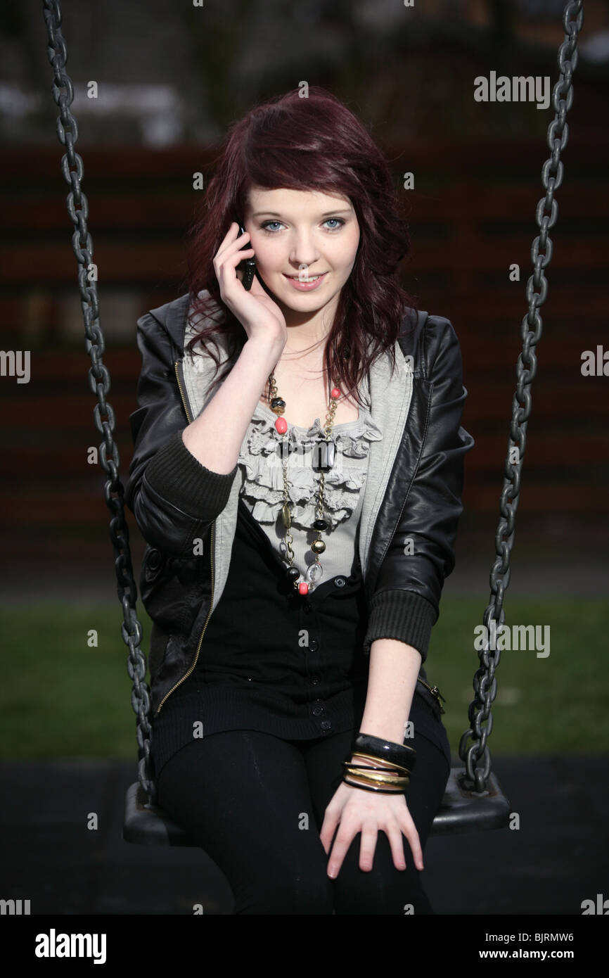 Teenage girl sitting on a swing in a park with a mobile phone held to her ear. Stock Photo
