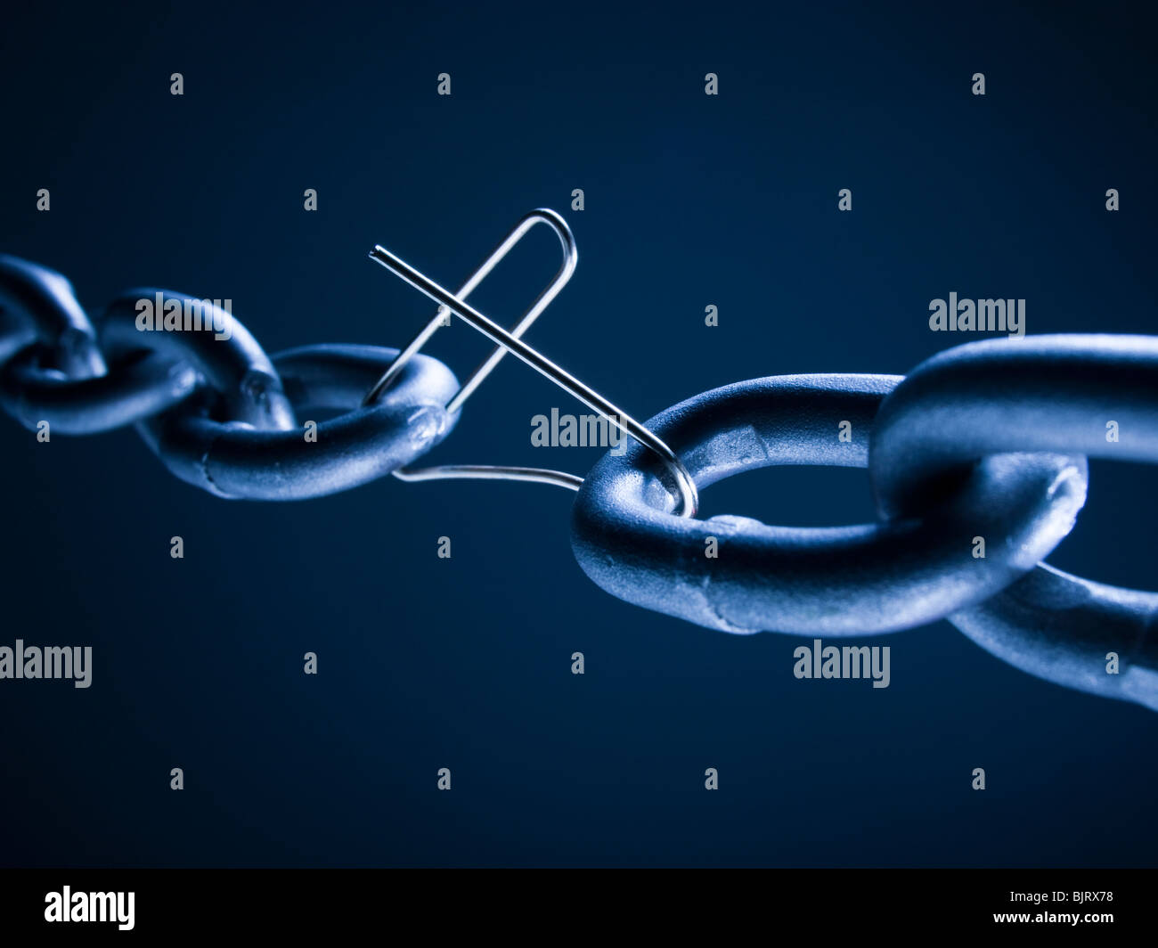 Chain linked with broken paper clip against blue background Stock Photo
