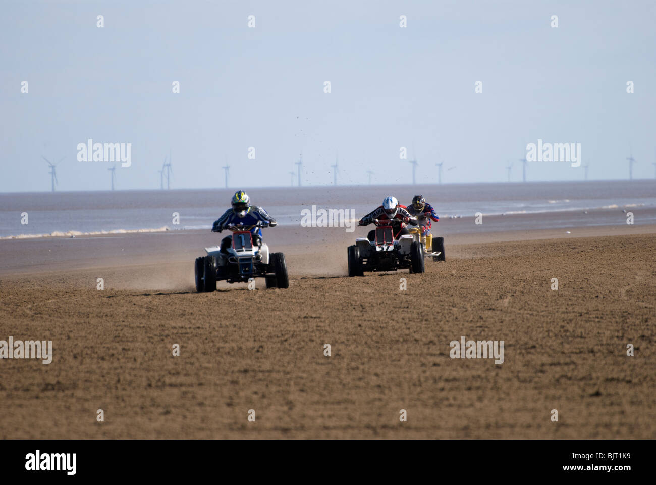 Quad bikes sand racing on the beach with wind turbines in the background out at sea, Mablethorpe, Lincolnshire, England, UK Stock Photo