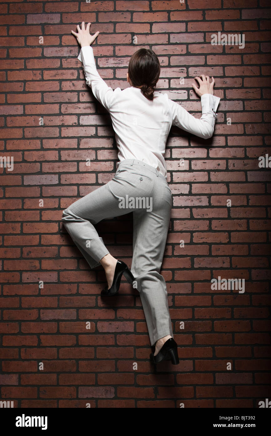 Studio shot of young woman climbing up brick wall Stock Photo