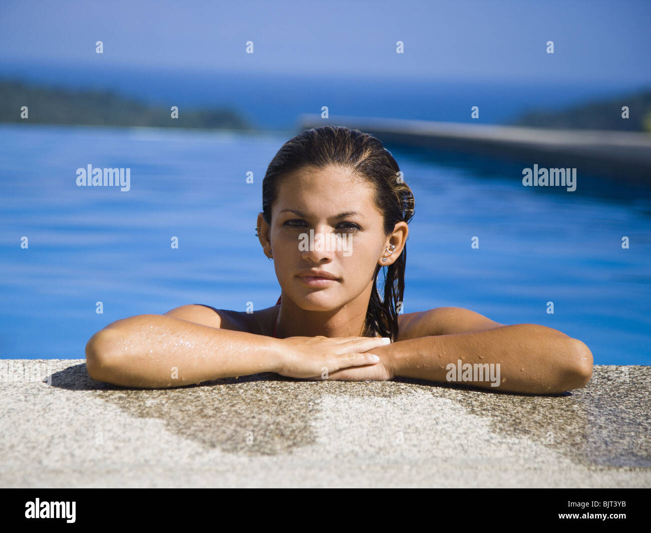 Woman resting on ledge of swimming pool Stock Photo