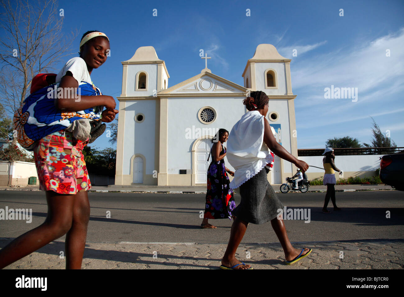 Women carrying their children past a church in the bay of Namibe, Namibe Province, Angola, Africa Stock Photo