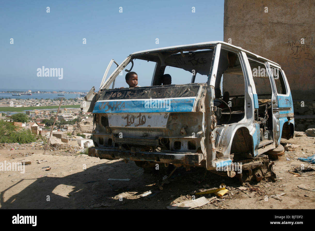 Child playing in remains of a stripped down minibus taxi. Barrio area on the hills north of Lobito. Benguela Province. Angola. A Stock Photo
