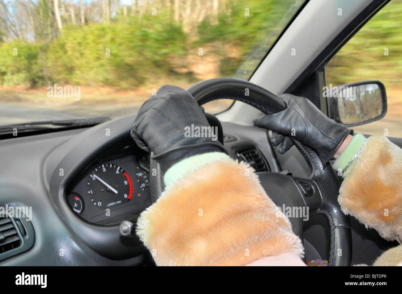 A close up of a woman 's hand on the steering wheel of a car. She wears