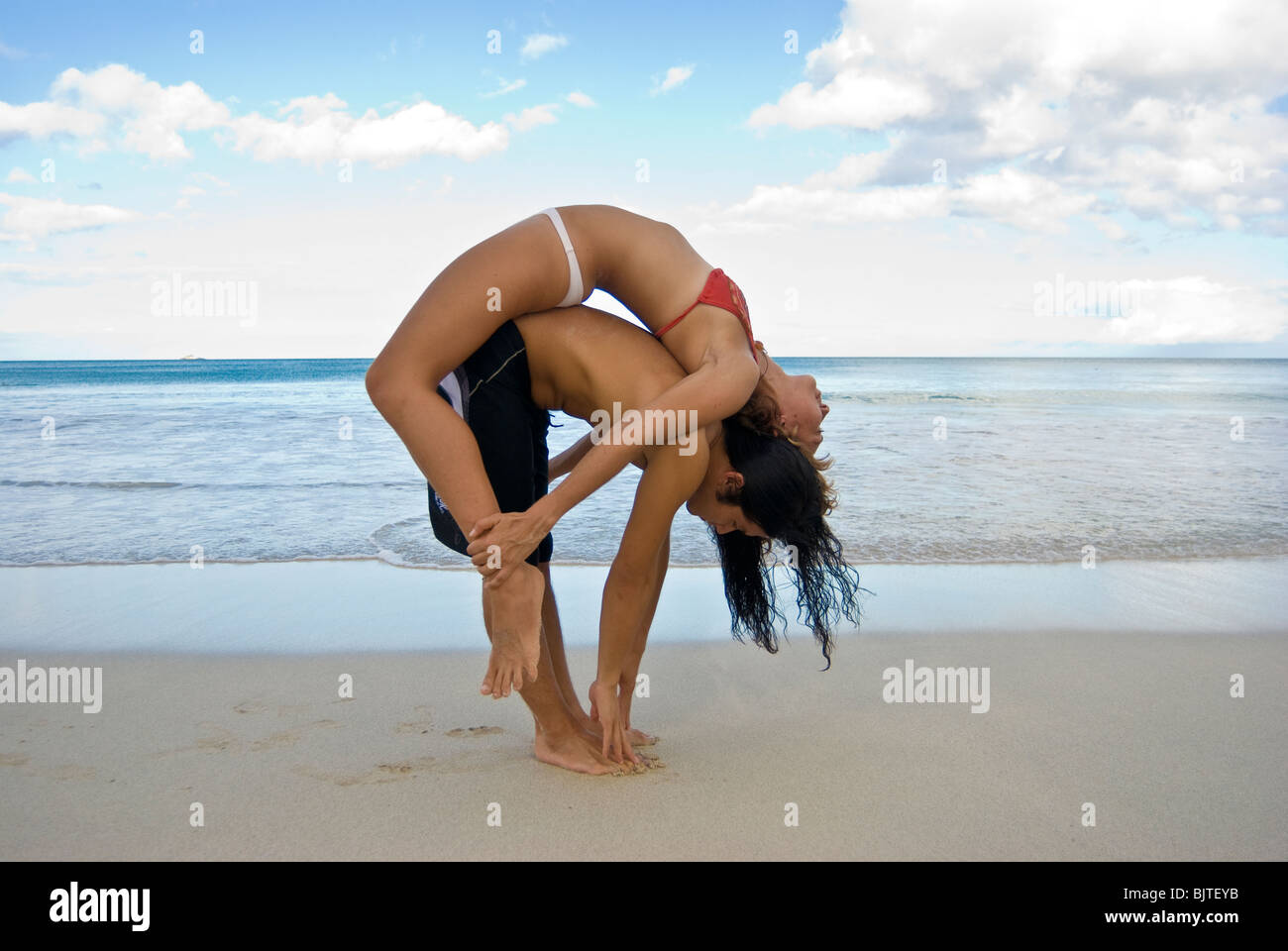 Young couple ( Asian man and Caucasian woman) in early twenties doing partner yoga on white sand beach in Hawaii Stock Photo