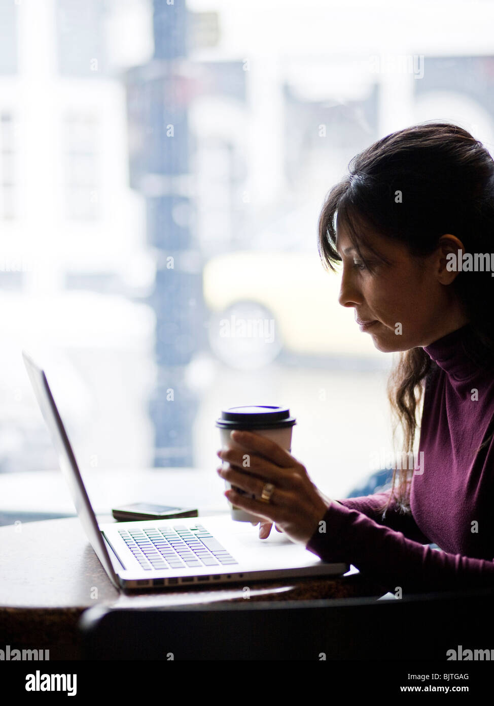 One mid adult woman drinking coffee next to laptop in cafe Stock Photo
