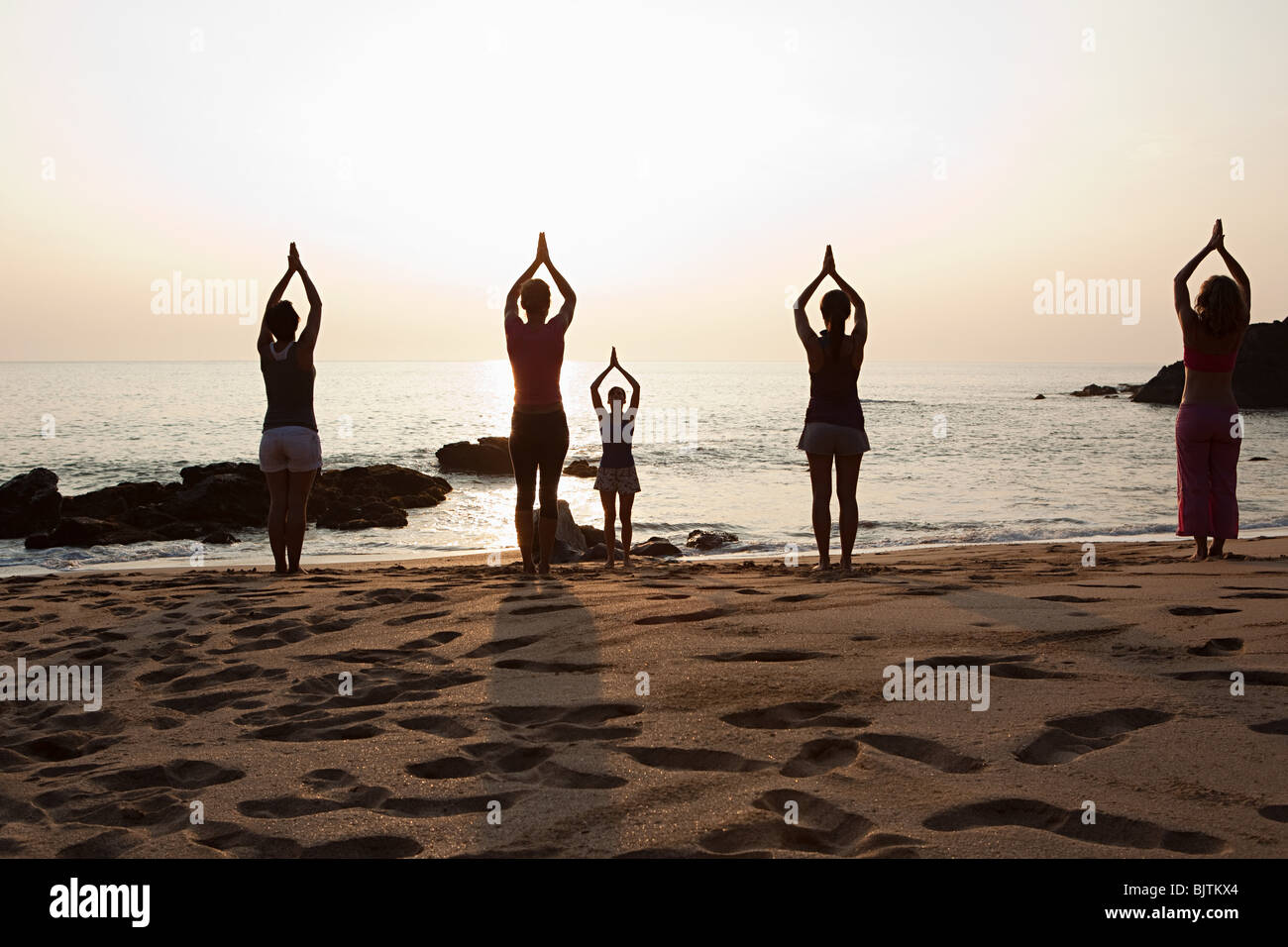 Women practicing yoga on beach at sunset Stock Photo