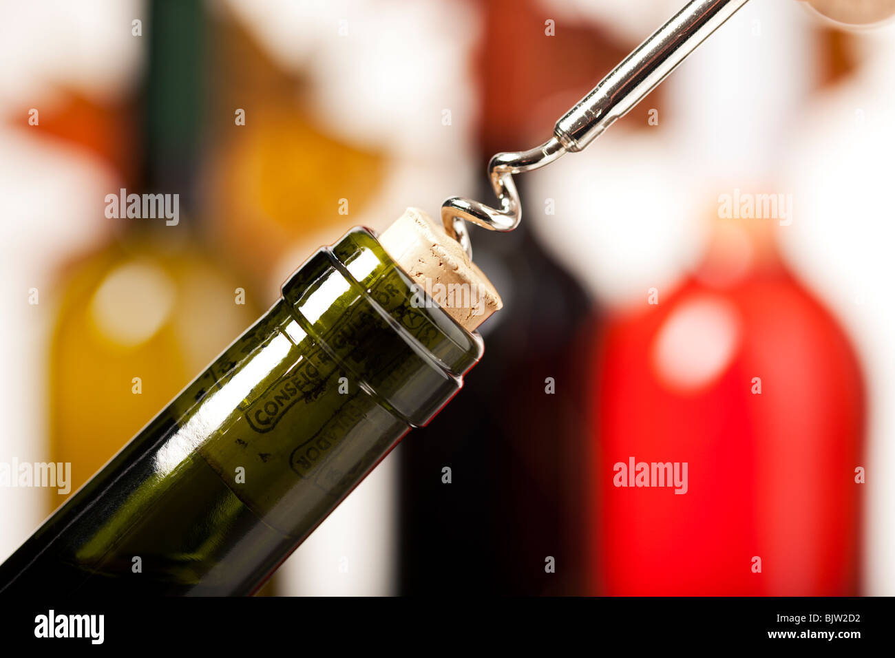 opening a bottle of Rioja wine with a corkscew, closeup, blurred wine bottles in background Stock Photo