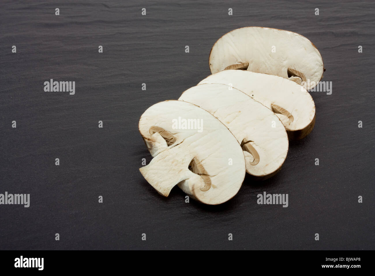 Sliced and whole Chestnut Mushrooms on background of dark slate. Stock Photo