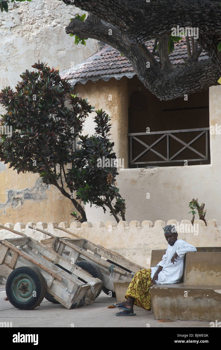 A man sits in Lamu's main square in front of the old fort, Northern Kenya, Africa Stock Photo