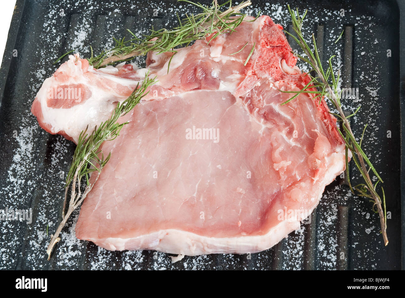 raw pork chop on a griddle with salt and rosemary ready to be cooked Stock Photo