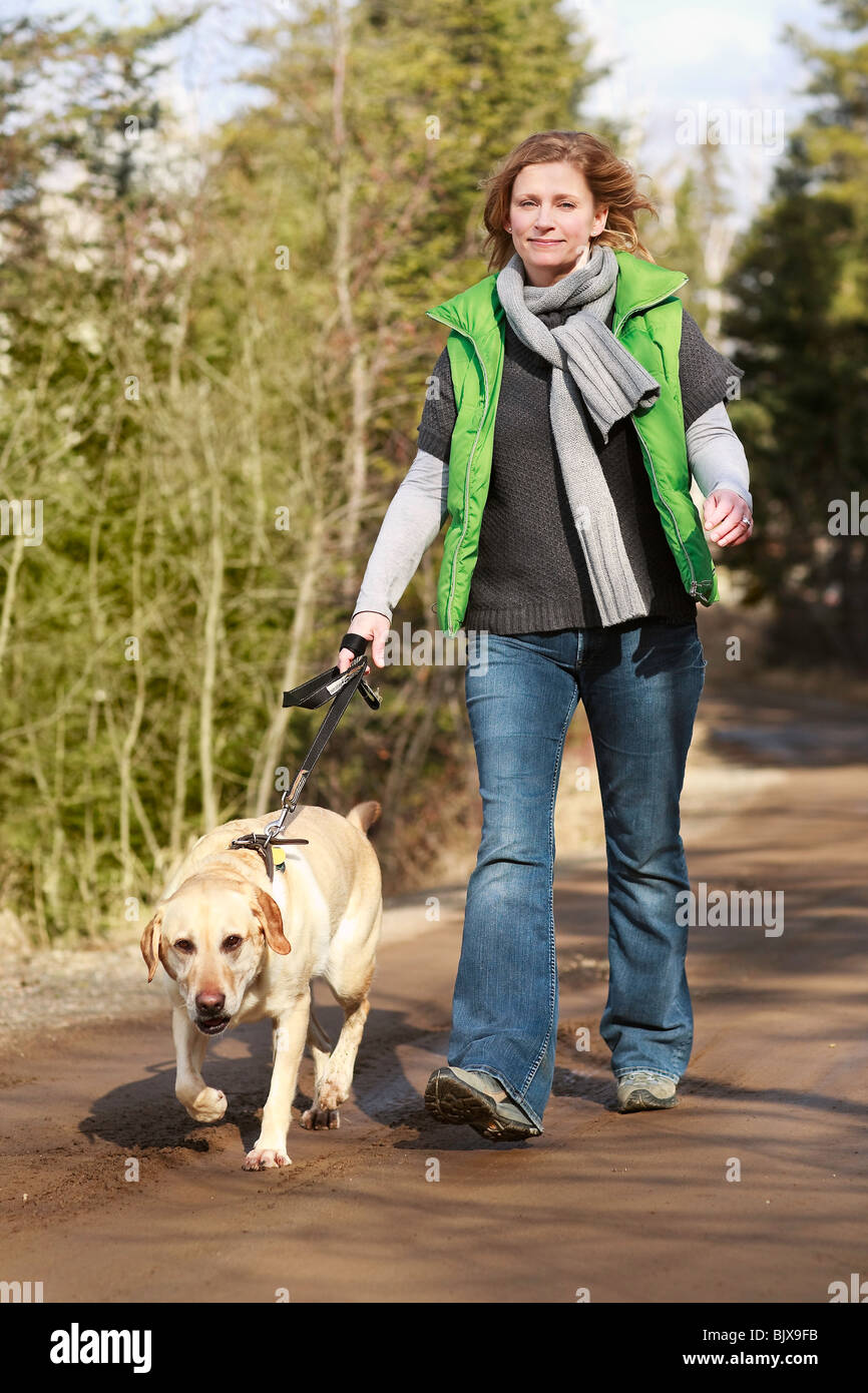 Woman walking her Yellow Labrador Retriever on a rural road, Trout Lake, Ontario, Canada. Stock Photo