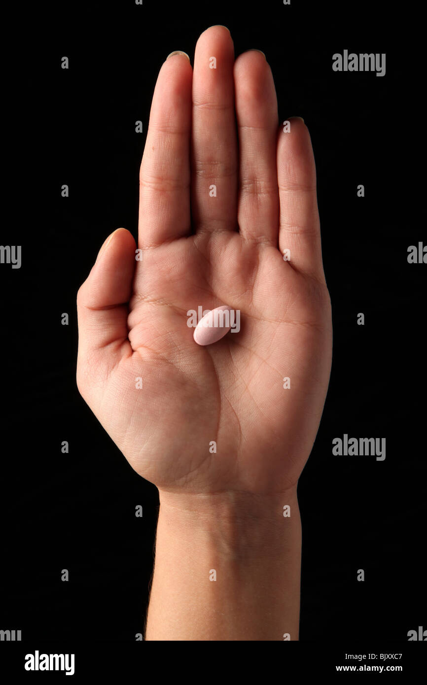 A female woman's hand holding one pill in the palm of her hand Stock Photo
