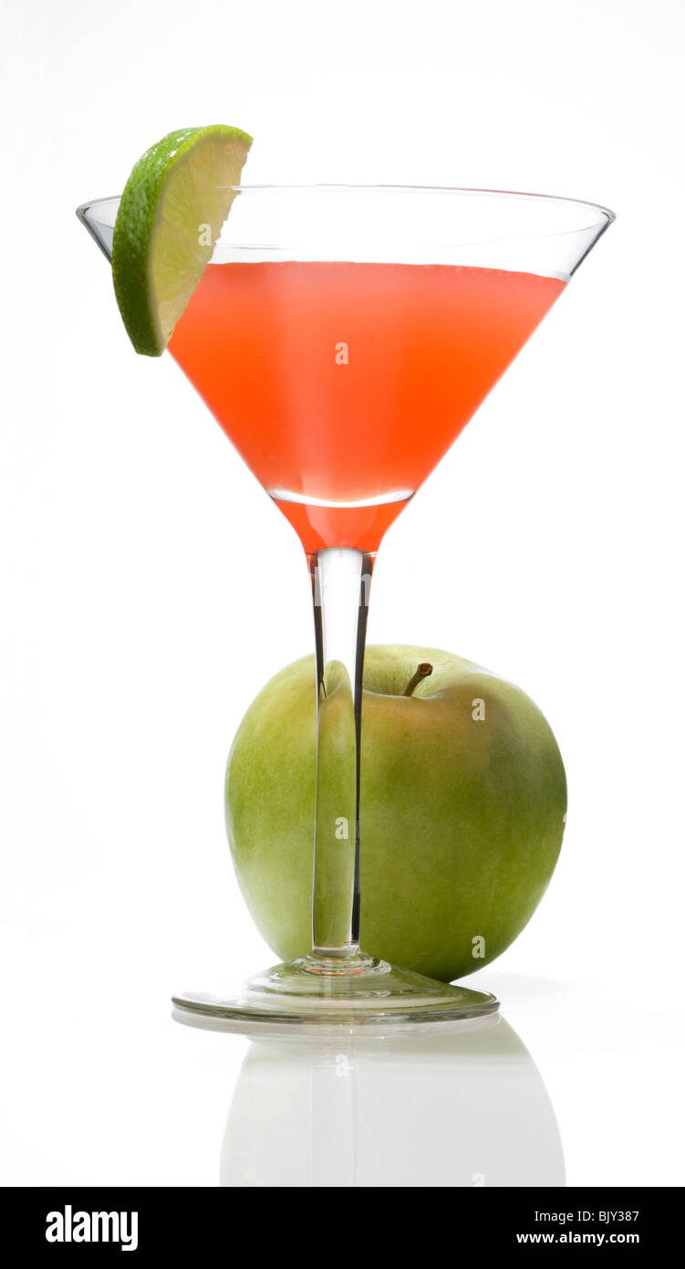 A cocktail glass with a mixed drink, whole green apple and a lime wedge garnish on the rim of the glass Stock Photo