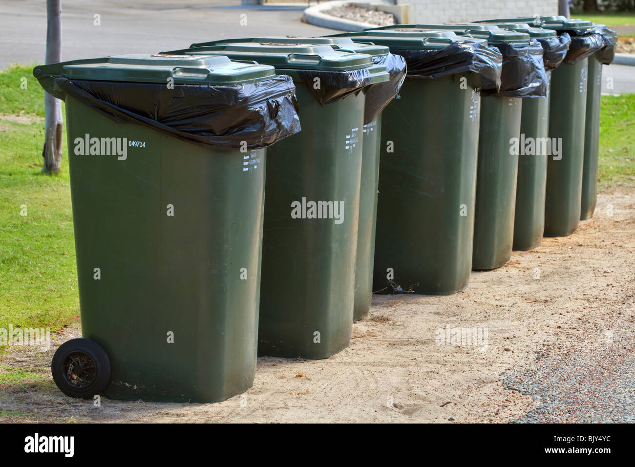 Row of wheelie bins waiting for pickup. Green bins for household refuse waiting beside the road. Stock Photo