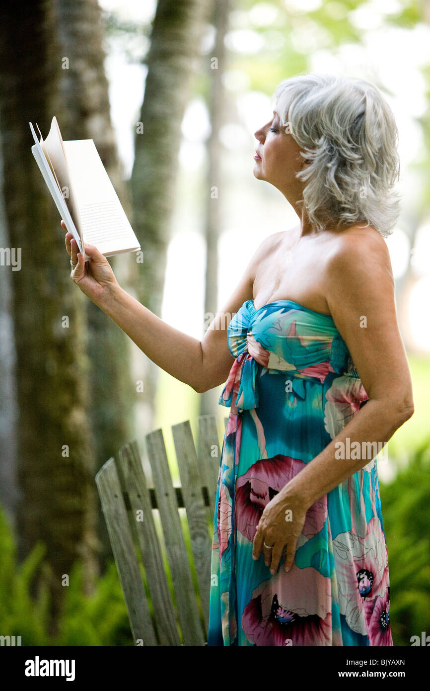 Middle-aged woman in strapless dress reading book in garden Stock Photo