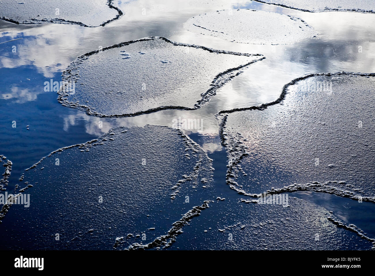 Thin ice breaking on a spring day, clouds and sky reflected in the