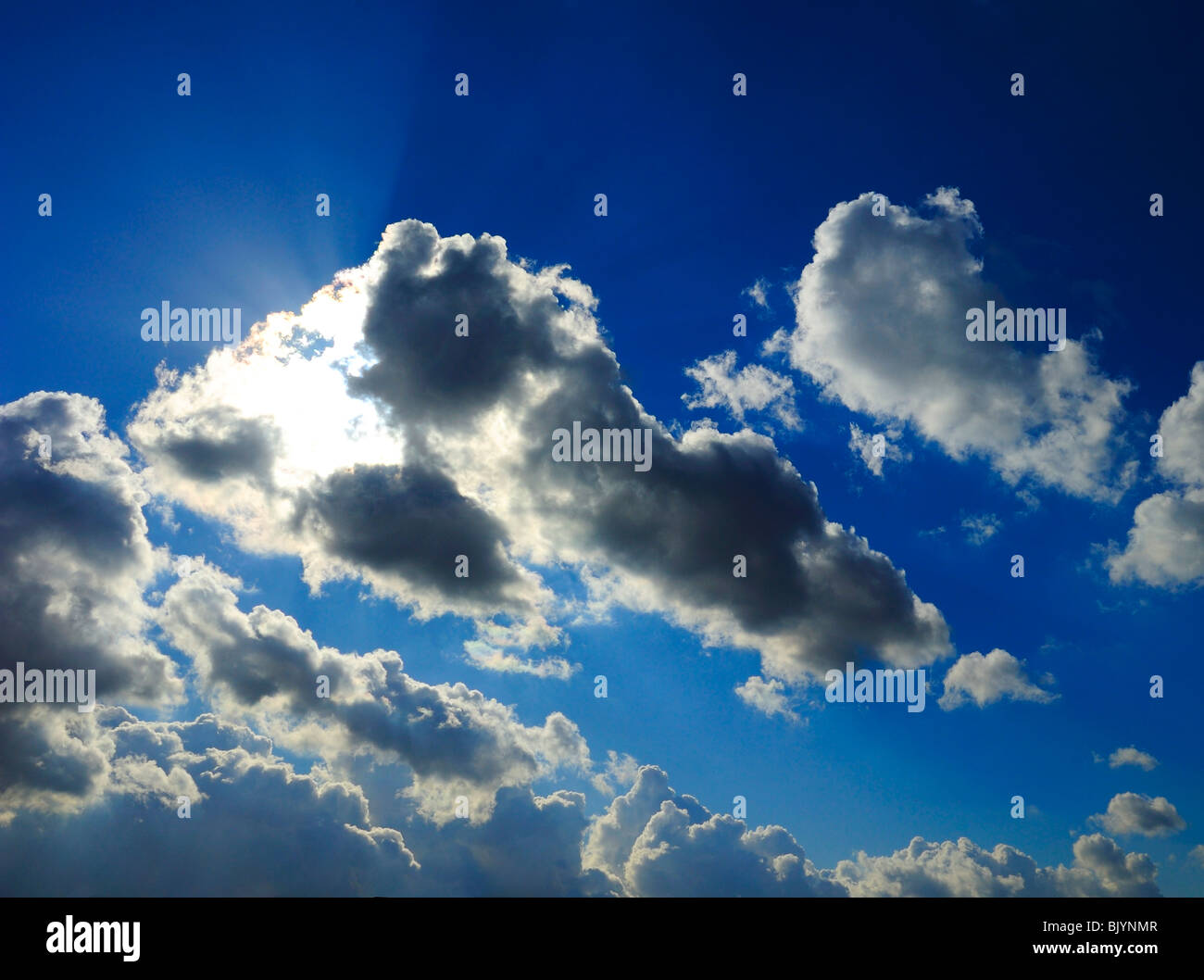 sun covered by pretty clouds in clear blue sky, projecting remarkable colorful beams Stock Photo