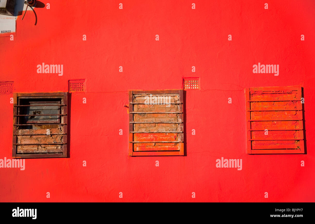 Red wall with 3 windows with steel bars Stock Photo