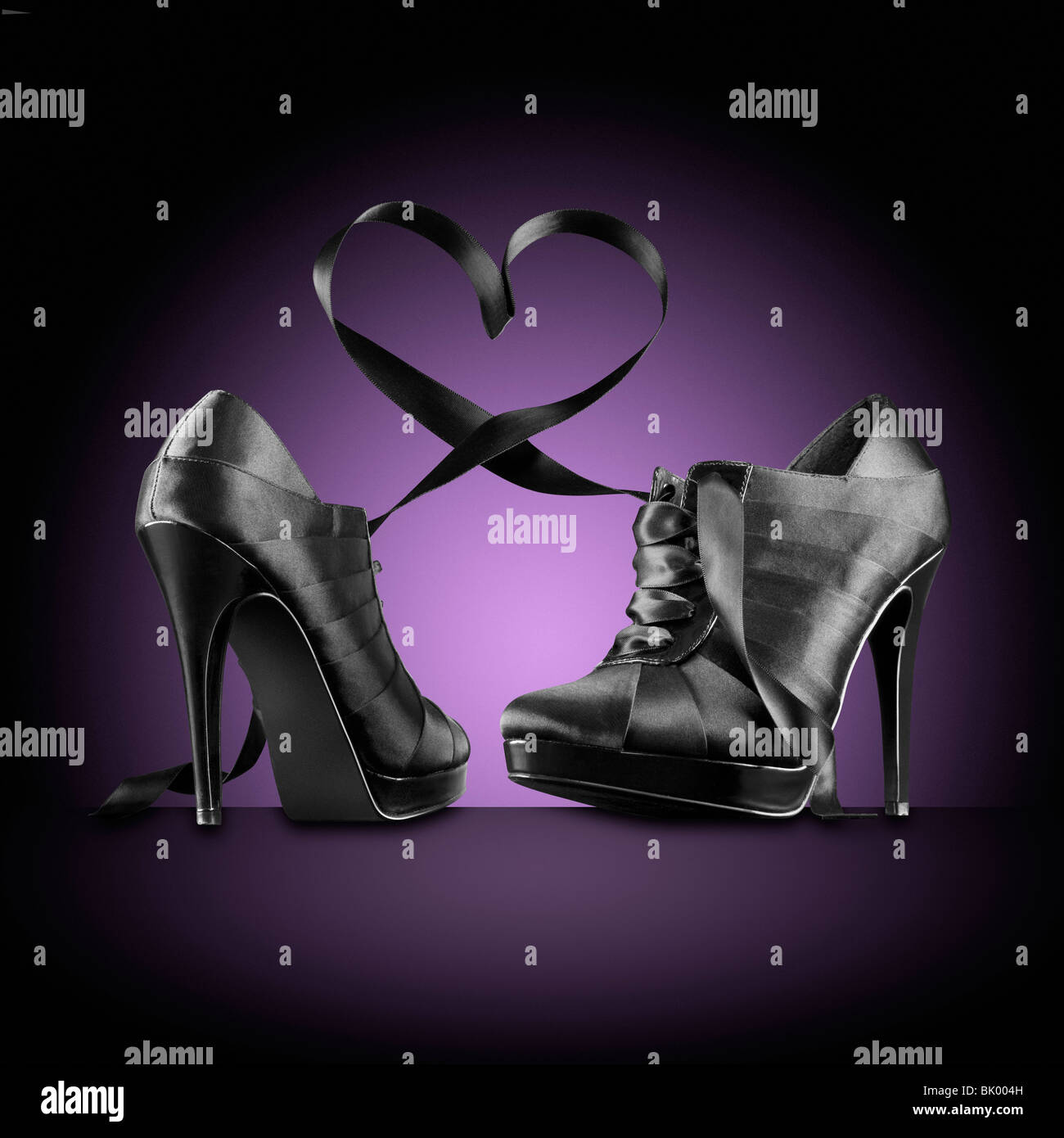 Very high black stiletto heels with the laces forming a heart shape above the shoes. The background is purple with a pool of light behind the shoes. Stock Photo