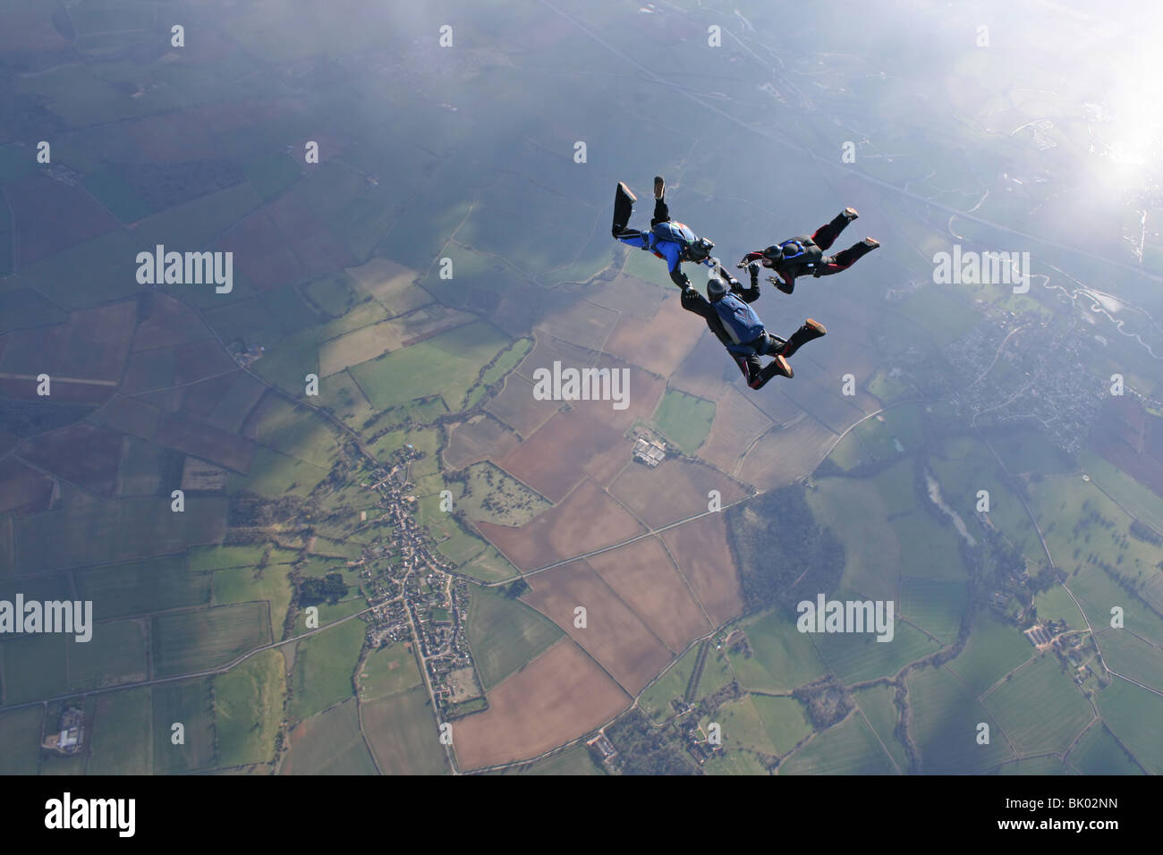 Three skydivers in free fall with the sun lightning up the earth below Stock Photo