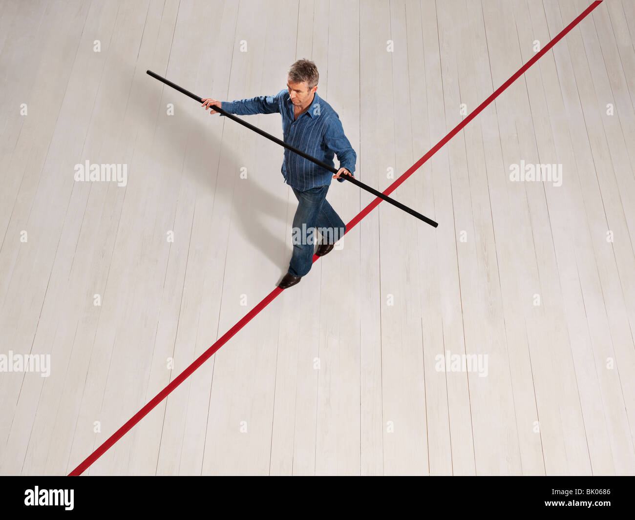 Man balancing on thin red line with pole Stock Photo