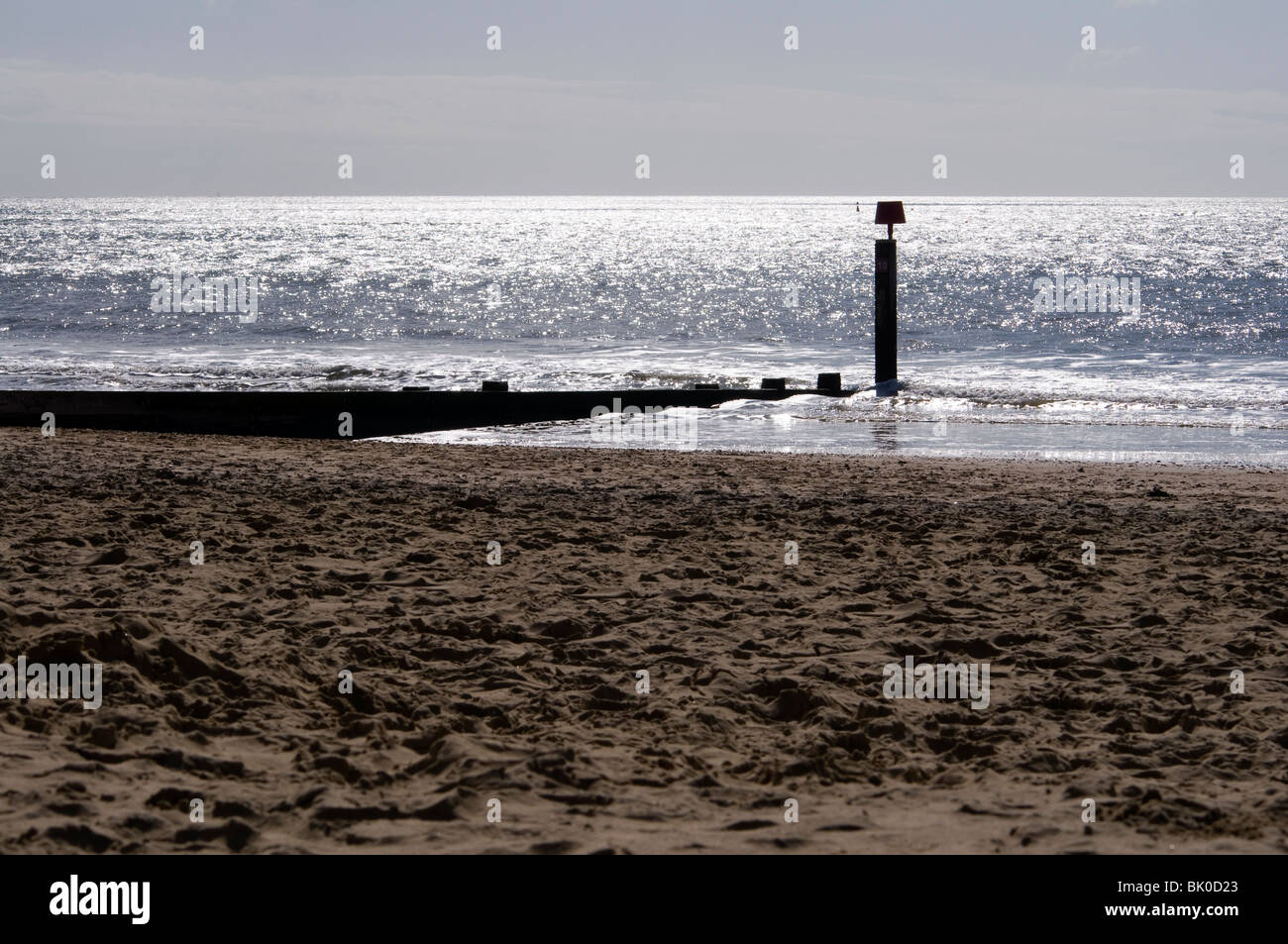 A groyne and beach marker in Bournemouth with the sun glinting off the sea. Stock Photo