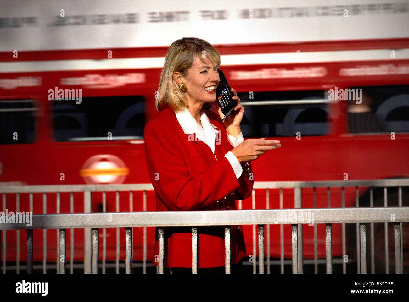 LIFESTYLE FASHION TECHNOLOGY 1980s  MOTOROLA FLIP PHONE 1980's advertising image illustrating business executive woman talking with London red bus speed blurred behind with early first generation flip open mobile cell telephone London UK Stock Photo